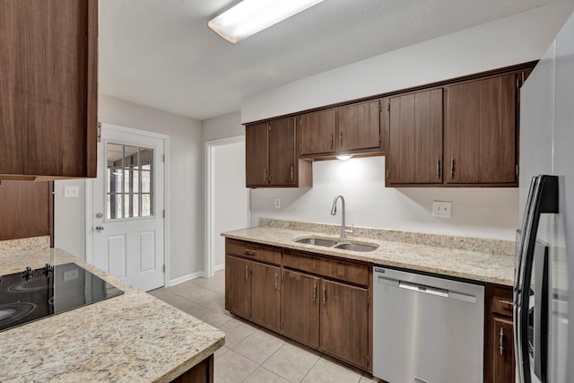 kitchen with light stone countertops, dark brown cabinetry, light tile patterned floors, stainless steel appliances, and a sink