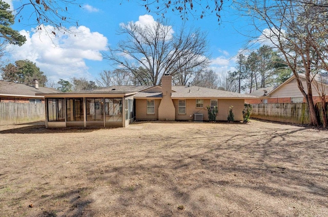 back of property featuring brick siding, central AC, a chimney, a fenced backyard, and a sunroom