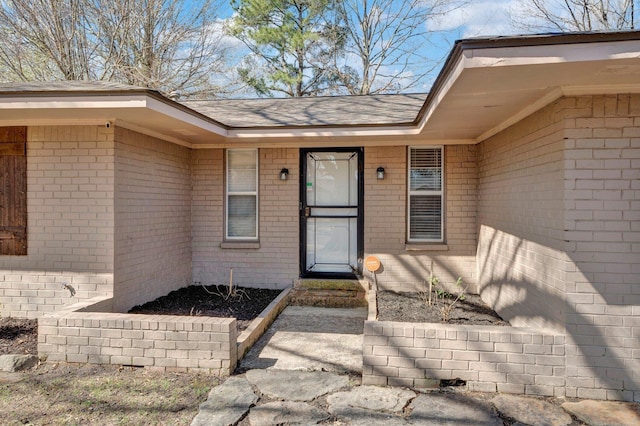 doorway to property featuring brick siding and a shingled roof