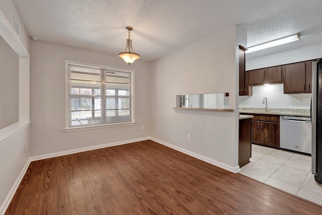 kitchen featuring a sink, light countertops, dark brown cabinets, stainless steel dishwasher, and light wood-type flooring