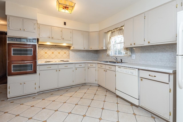 kitchen featuring under cabinet range hood, a sink, white appliances, light countertops, and decorative backsplash