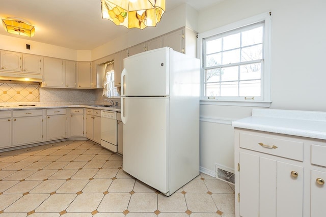 kitchen with tasteful backsplash, visible vents, under cabinet range hood, light countertops, and white appliances