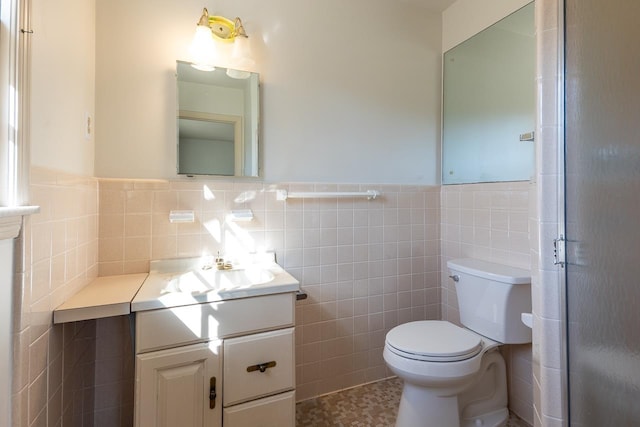 bathroom with a wainscoted wall, toilet, tile walls, and vanity