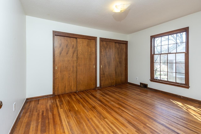 unfurnished bedroom featuring wood finished floors, visible vents, baseboards, multiple closets, and a textured ceiling