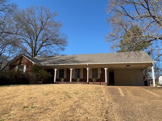 ranch-style house with an attached carport, a front yard, and dirt driveway