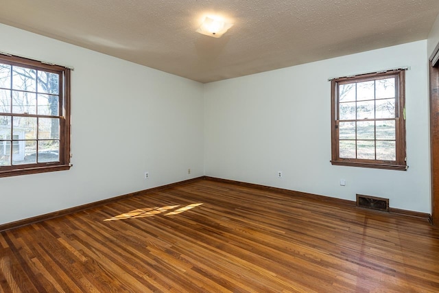 spare room with a wealth of natural light, visible vents, dark wood-type flooring, and a textured ceiling