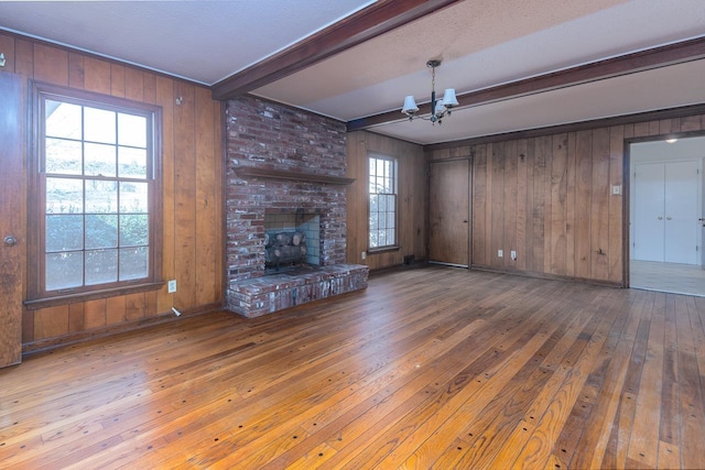 unfurnished living room featuring hardwood / wood-style floors, beam ceiling, a fireplace, wood walls, and a chandelier