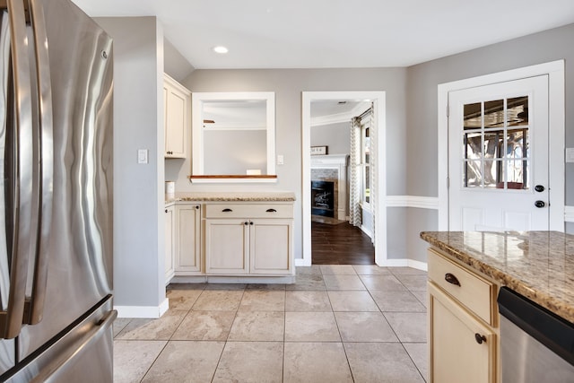 kitchen featuring stainless steel appliances, a fireplace, light tile patterned floors, baseboards, and light stone countertops