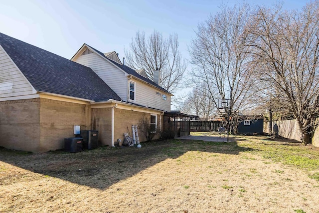 view of property exterior with a lawn, fence, roof with shingles, brick siding, and a chimney