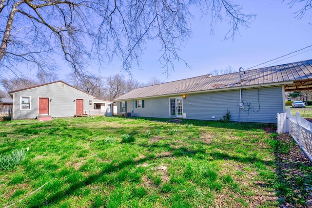 rear view of house with fence, entry steps, a lawn, french doors, and metal roof