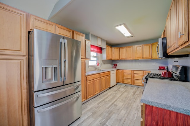 kitchen with a sink, stainless steel appliances, light brown cabinetry, and light wood finished floors