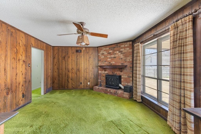 unfurnished living room featuring carpet flooring, wooden walls, plenty of natural light, and a wood stove