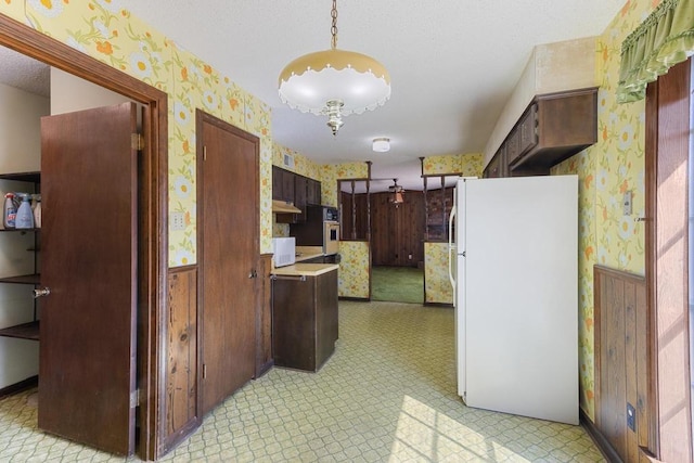 kitchen with light floors, wainscoting, freestanding refrigerator, and wallpapered walls