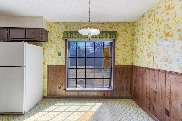 unfurnished dining area with a textured ceiling, wood walls, wainscoting, wallpapered walls, and light floors