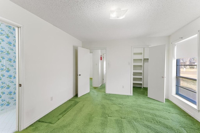 unfurnished bedroom with a walk in closet, light colored carpet, baseboards, and a textured ceiling