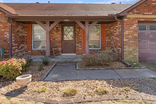 view of exterior entry featuring brick siding, a garage, and roof with shingles