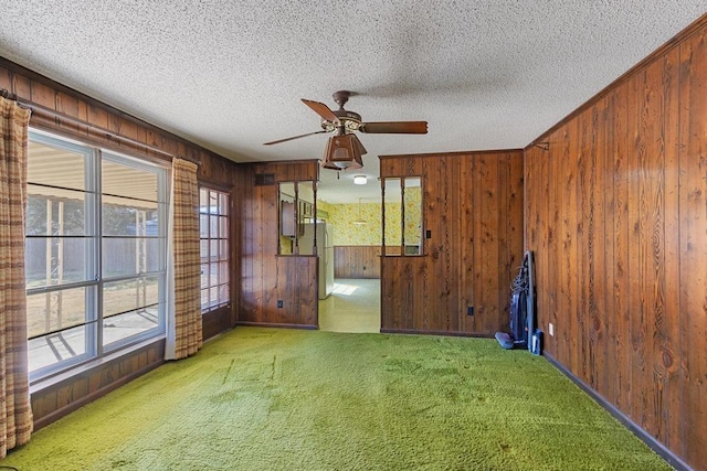 carpeted spare room featuring a ceiling fan, wood walls, and a textured ceiling