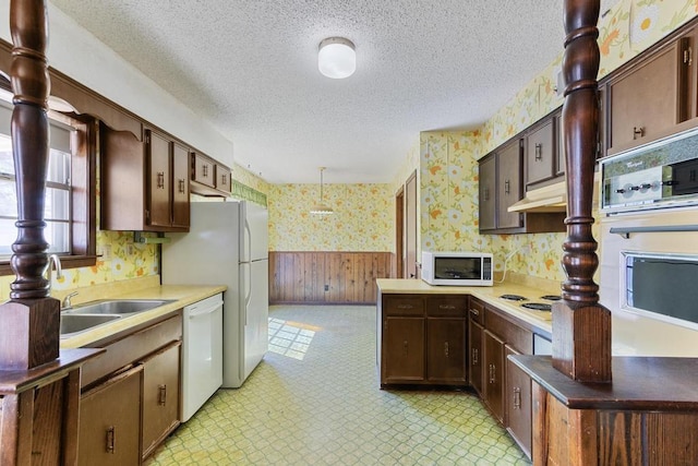 kitchen featuring wallpapered walls, light floors, wainscoting, white appliances, and a textured ceiling