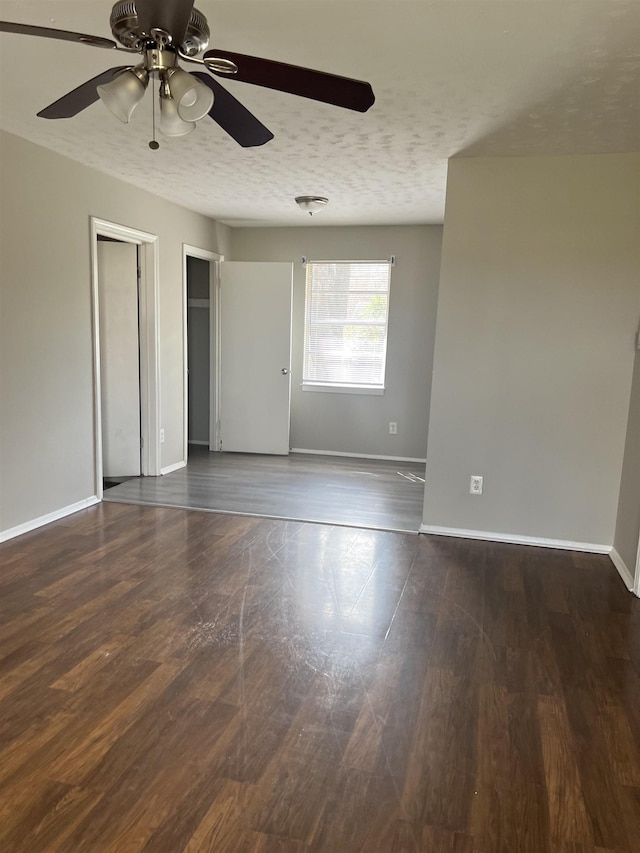 empty room featuring baseboards, a textured ceiling, ceiling fan, and dark wood finished floors