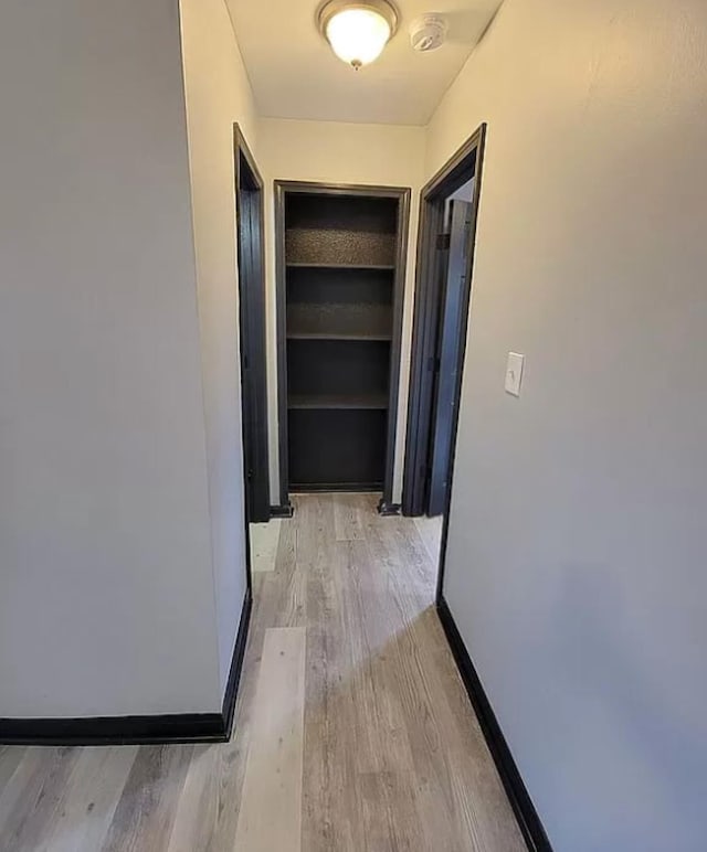 corridor with light wood-type flooring and baseboards