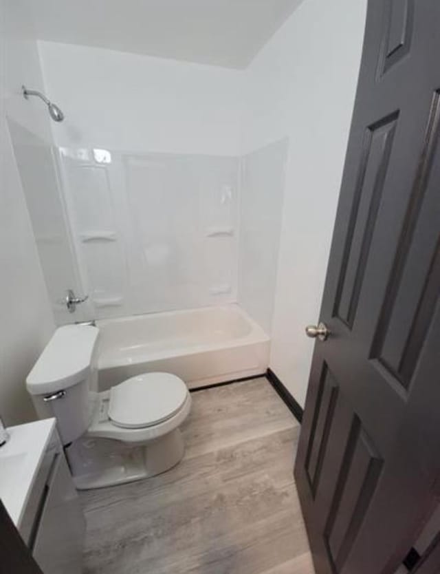 bathroom with toilet, wood finished floors, shower / bath combination, baseboards, and vanity