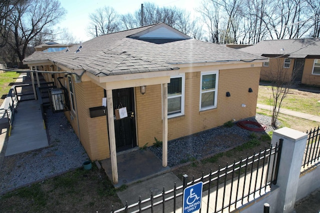 exterior space with a fenced front yard, brick siding, and a shingled roof