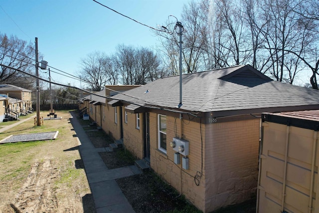 view of side of property featuring a lawn, brick siding, and roof with shingles