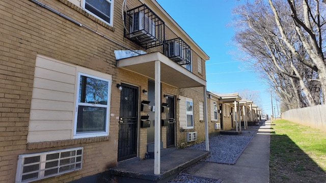 exterior space with brick siding, a balcony, and fence