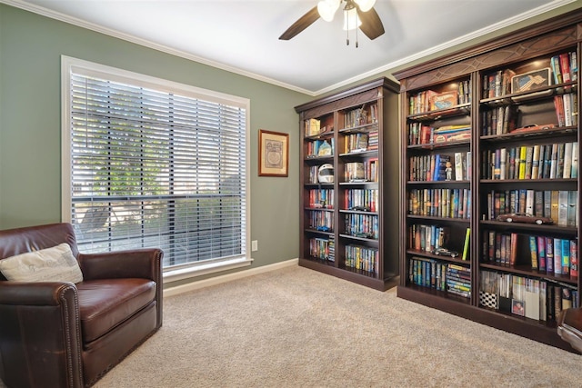 living area featuring baseboards, ceiling fan, bookshelves, carpet floors, and ornamental molding