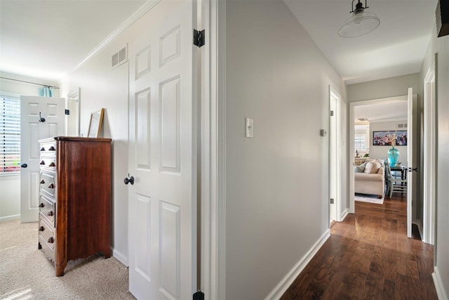 corridor featuring visible vents, baseboards, wood finished floors, and ornamental molding