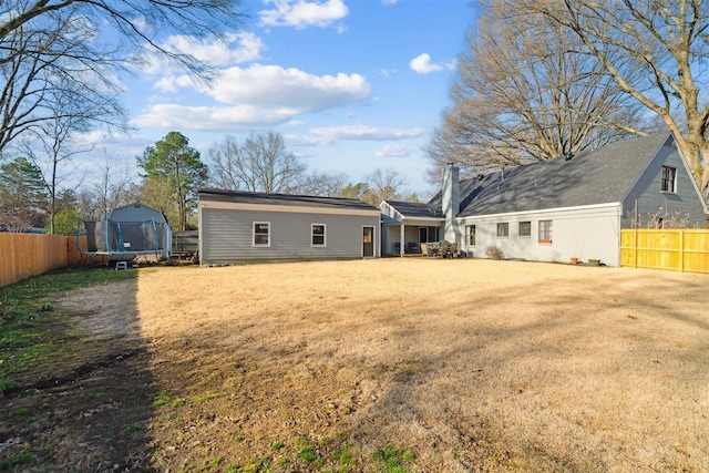 rear view of house featuring a fenced backyard, a lawn, and a trampoline