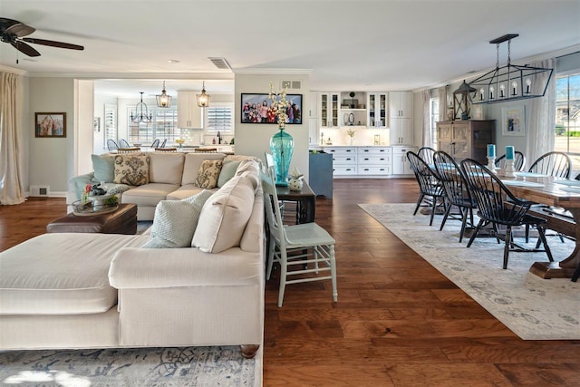 living room featuring visible vents, dark wood-style floors, ornamental molding, and ceiling fan with notable chandelier