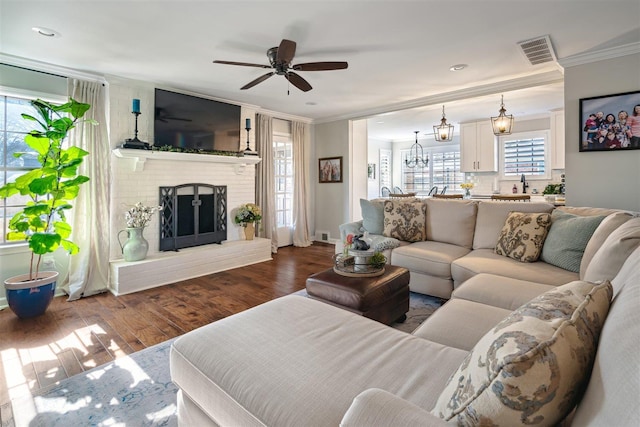 living area featuring wood finished floors, visible vents, a fireplace, ceiling fan, and ornamental molding