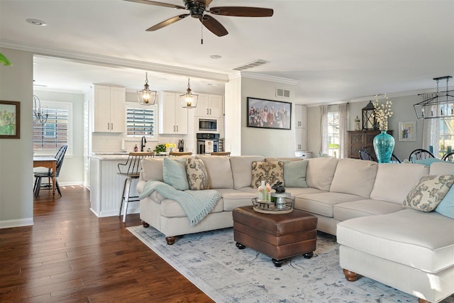 living area featuring visible vents, dark wood-type flooring, crown molding, and ceiling fan with notable chandelier