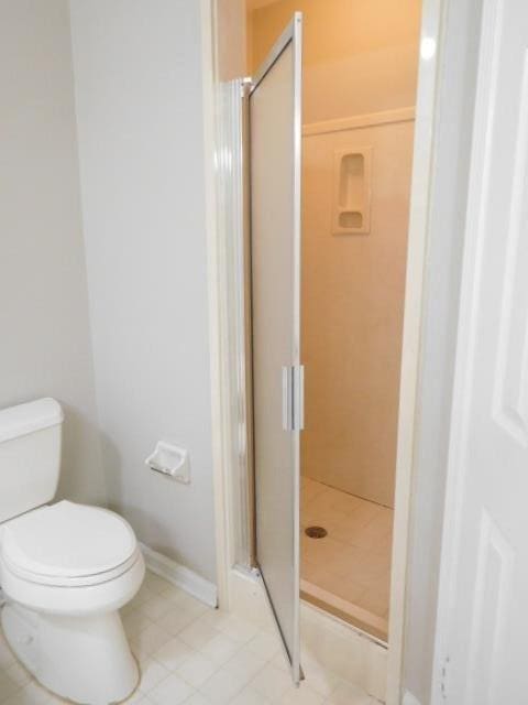 bathroom with baseboards, toilet, and a shower stall