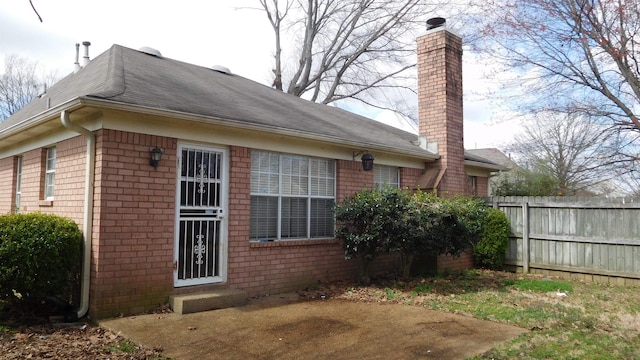 view of side of property featuring brick siding, a chimney, and fence