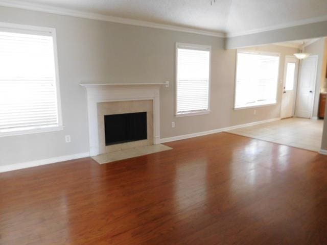 unfurnished living room with baseboards, a fireplace with flush hearth, vaulted ceiling, ornamental molding, and wood finished floors