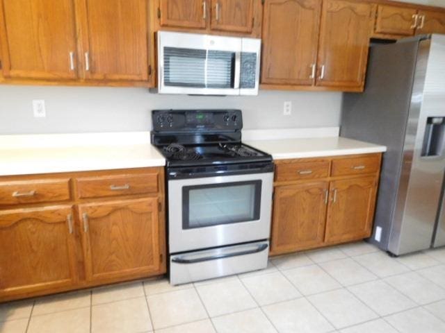 kitchen featuring brown cabinetry, light tile patterned floors, stainless steel appliances, and light countertops