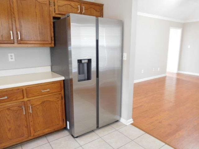 kitchen with brown cabinets, stainless steel fridge, crown molding, light countertops, and light tile patterned floors