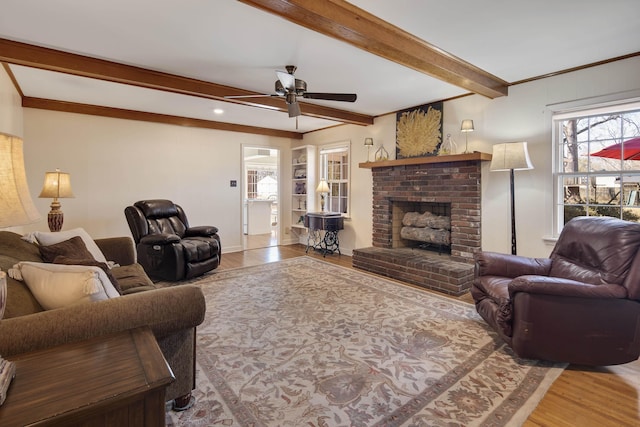 living room with beamed ceiling, a fireplace, ceiling fan, and wood finished floors