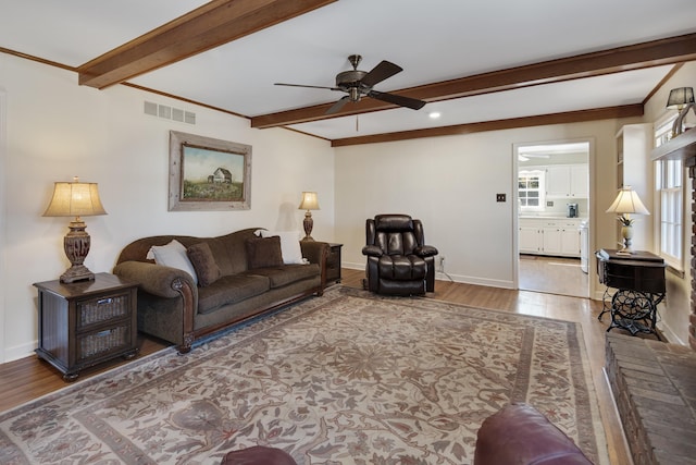 living area with visible vents, beamed ceiling, a ceiling fan, wood finished floors, and baseboards