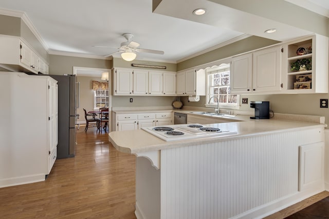 kitchen featuring a peninsula, ornamental molding, light wood finished floors, and a sink