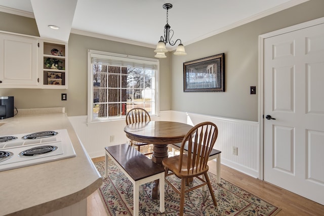 dining space featuring a wainscoted wall, light wood-style floors, a chandelier, and ornamental molding