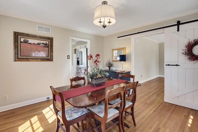 dining room featuring visible vents, a barn door, ornamental molding, and light wood-style flooring