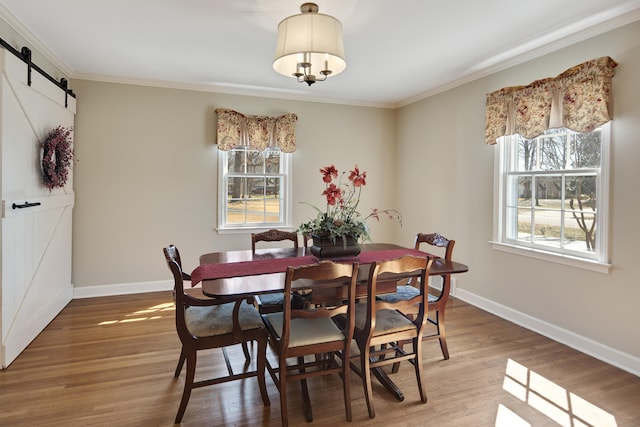 dining area with a barn door, wood finished floors, baseboards, and ornamental molding