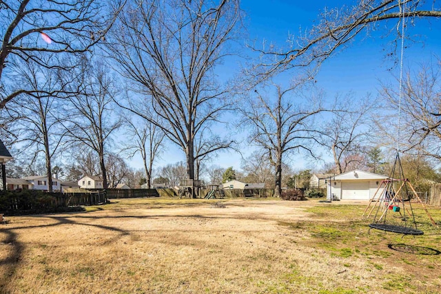 view of yard featuring a detached garage, fence, and playground community