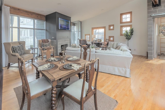 dining room featuring a fireplace, light wood finished floors, and high vaulted ceiling