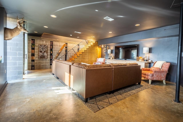 living area featuring concrete block wall, visible vents, concrete floors, recessed lighting, and stairs