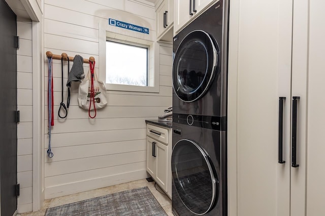 laundry area with wooden walls, cabinet space, and stacked washer / drying machine