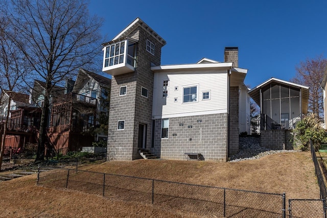 back of property with a chimney, entry steps, fence private yard, and a sunroom